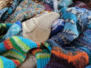 Wollsöckchen Viele selbstgestrickte bunte Wollsöckchen in verschiedenen Größen liegen in einem Korb.