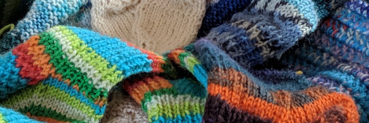 Viele selbstgestrickte bunte Wollsöckchen in verschiedenen Größen liegen in einem Korb.