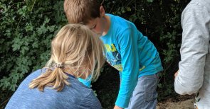 Kinder handwerken mit einer Säge. Sie sind draußen und die Sonne scheint.