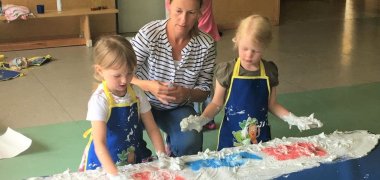 Zwei etwa dreijährige Mädchen und ihre Erzieherin malen mit Fingerfarben.