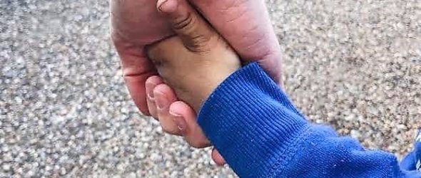Eine kleine Kinderhand liegt in der großen Hand eines Erwachsenen.