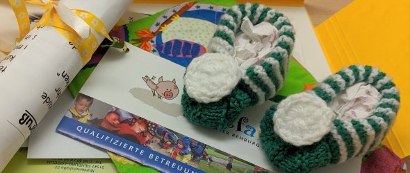 Eine gelbe Mappe liegt aufgeschlagen und den zeigt den Inhalt: Bunte Flyer, zum Teil gerollt und mit Bändchen, sowie gestrickte Babysöckchen.