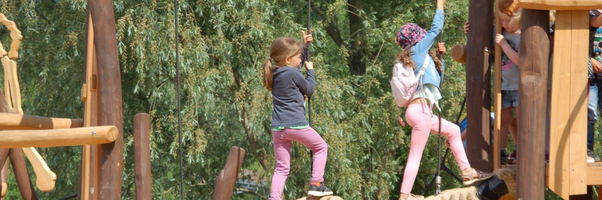 2  etwa 8-jährige Mädchen balancieren auf einem Klettergerüst aus Holz.