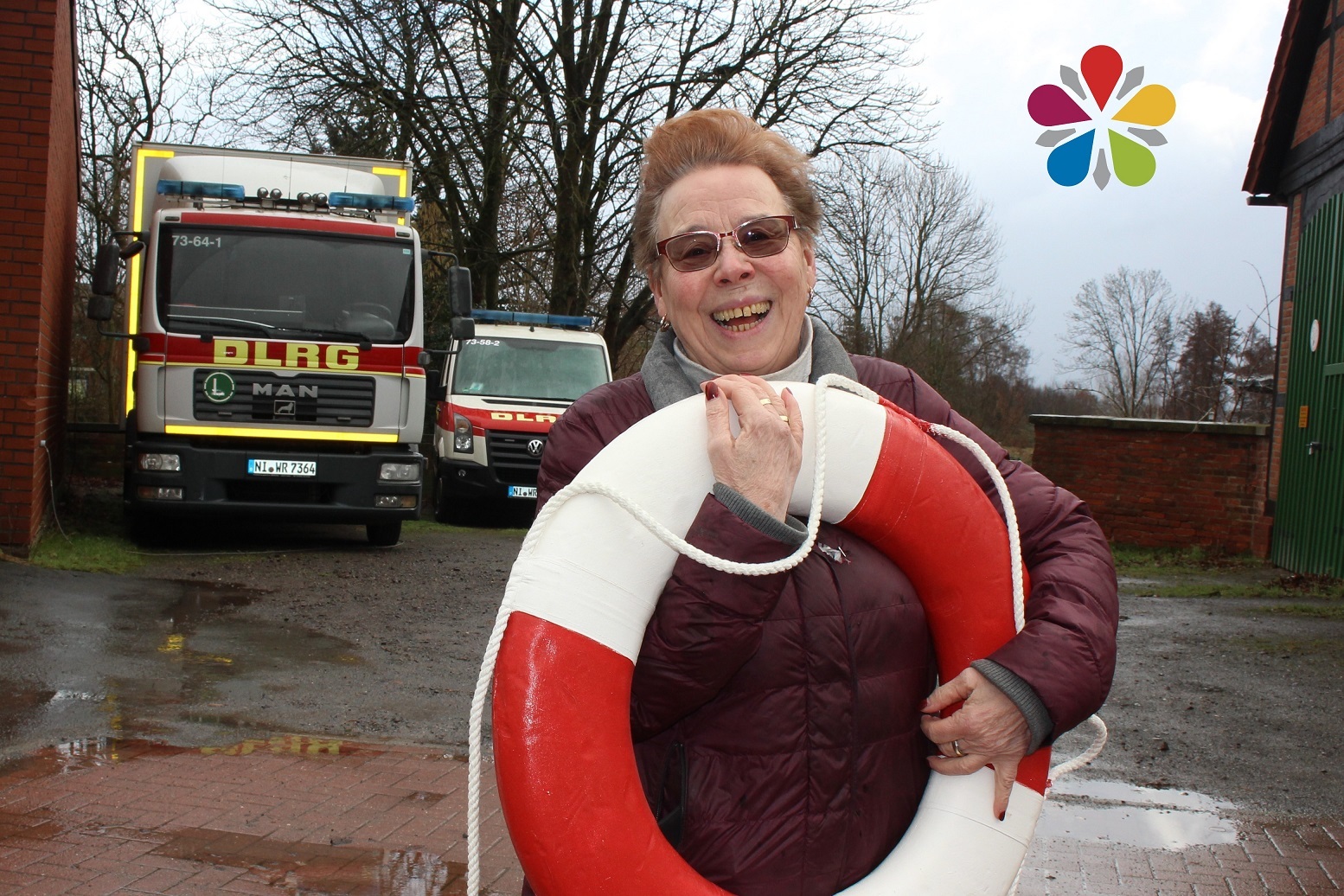 Angelika Teßner mit einen Rettungsring im Arm vor zwei DLRG Autos