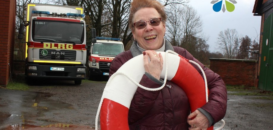 Angelika Teßner mit einen Rettungsring im Arm vor zwei DLRG Autos