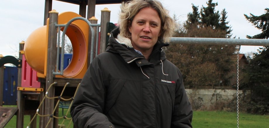 Frauke Kallendorf vor einem Spielplatz mit einem gelben Helm in der Hand